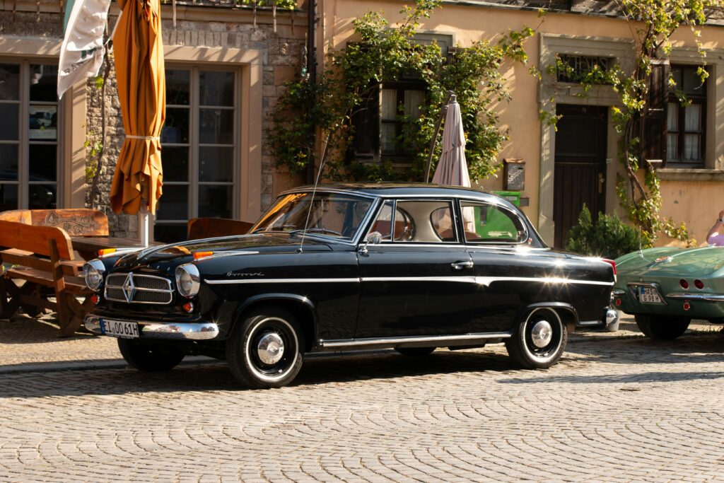 Black Borgward Isabella parked on a cobblestone street in a sunny city, highlighting its classic charm.